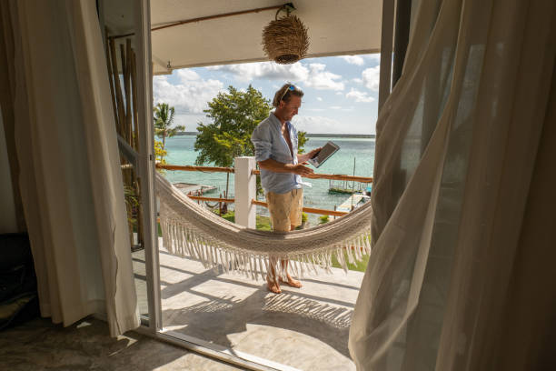 Young man relaxing in an hammock on a balcony using a digital tablet 30's man relaxing on hammock on upper floor balcony overlooking the beautiful lake of Bacalar, Mexico hammock men lying down digital tablet stock pictures, royalty-free photos & images