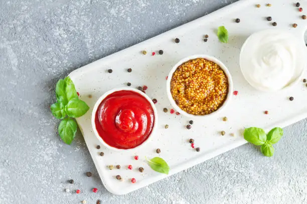 Photo of Popular sauces ketchup, dijon mustard and mayonnaise in bowls on tray top view