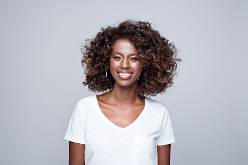 Headshot of happy, beautiful african young woman wearing white t-shirt, smiling at camera. Studio portrait on grey background.