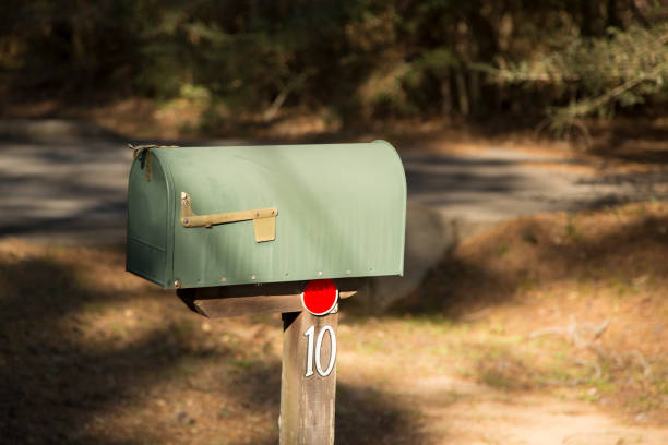 LV American style mailboxes on the side of road.   Single boxes in front of individual properties in wooded subdivisions. Mailboxes in rural community where each home furnishes their own mailbox.  These mailboxes are traditional black metal mailboxes with red flag.