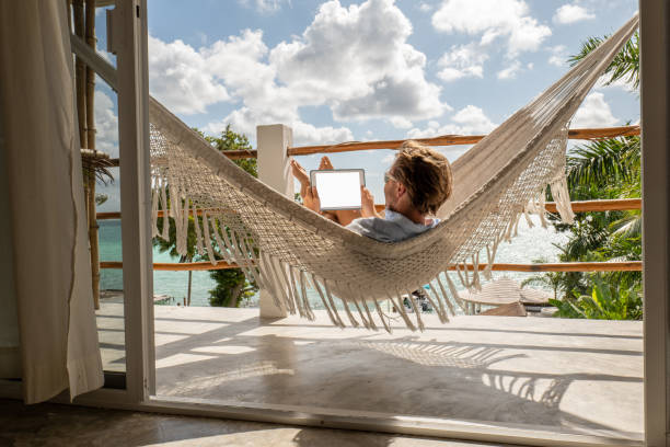 istock Young man relaxing in an hammock on a balcony using a digital tablet 1369781283