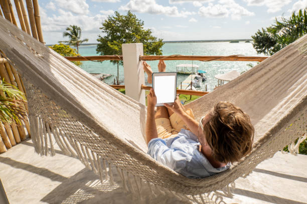 istock Young man relaxing in an hammock on a balcony using a digital tablet 1369781289