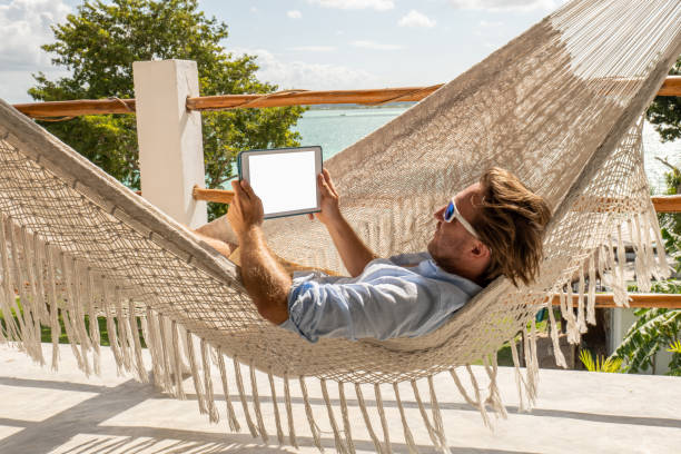istock Young man relaxing in an hammock on a balcony using a digital tablet 1369781323
