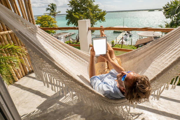 istock Young man relaxing in an hammock on a balcony using a digital tablet 1369781327