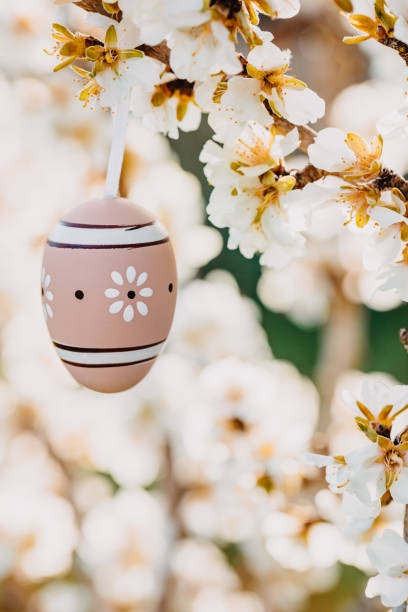 istock Close up of a beige boho easter egg hanging in between almond blossoms on an almond tree 1369789255