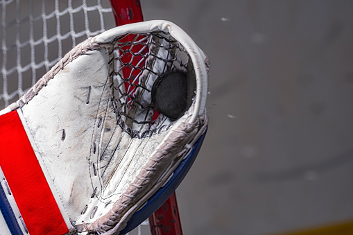 A close-up of an ice hockey puck being caught in the goalie’s glove in front of the goal net.
