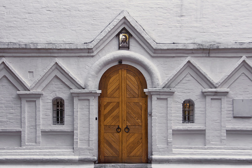 Wooden gate and two arched windows on a white brick wall. Entrance to the old christian church