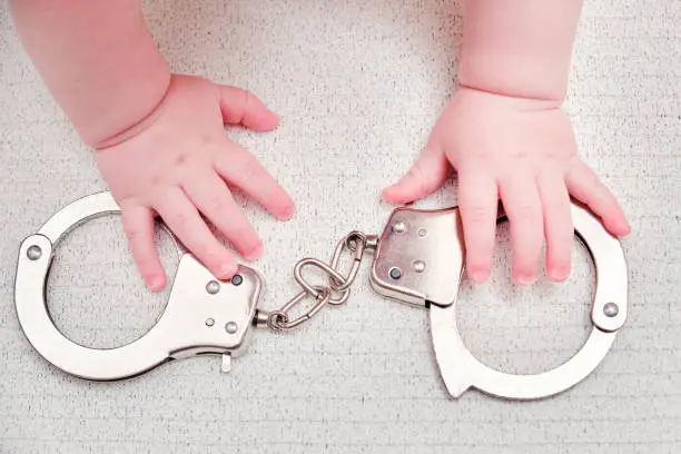 Photo of Baby hand and handcuffs, close-up. Children fingers and an object on a white background