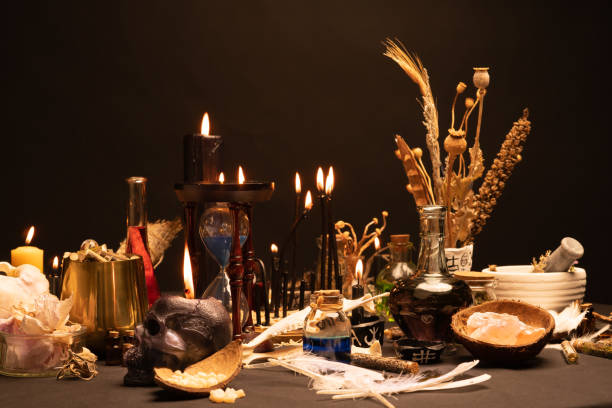 istock Witch ceremony with witch craft magic items. Selective focus at front. Still life with black magic skull candle, ritual human teeth and bird feathers, potion vials and sand clock or hourglass. Halloween. 1369795331