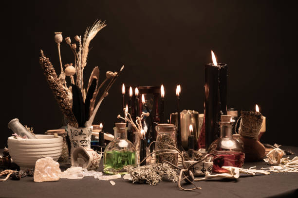 istock Occult and esoteric witch doctor still life. Selective focus. Halloween background with magic objects. Mortar and pestle, black candle, bones, crystal stones, and potions vials. Mystic witchery weeds. 1369795680