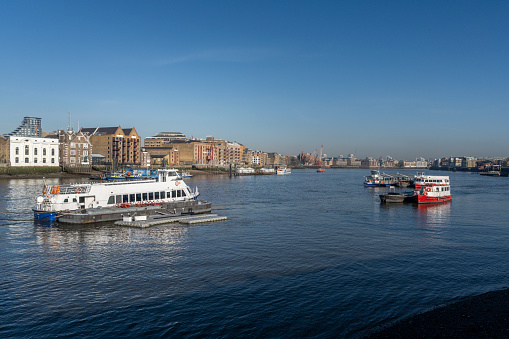 Boats and ferries on the Thames on a beautiful sunny day. In the background, apartment buildings in Wapping, London.