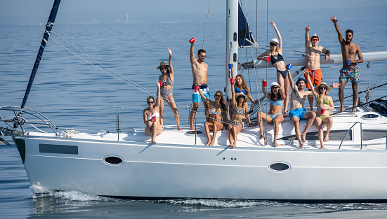 Large group of friends sailing and having fun on boat in summer. They toasting with raised glasses. Youth and lifestyle concept.