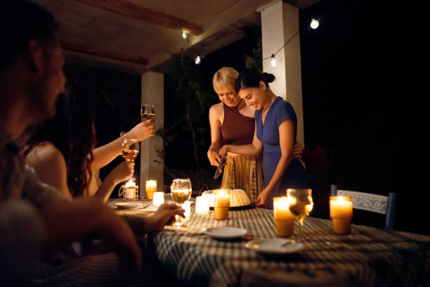 istock Charming lesbian couple, cutting their wedding cake, while their friends toasting to them 1369800470