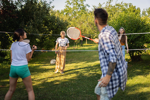 Carefree friends playing badminton, during summer day in the garden