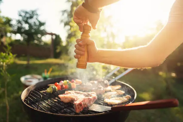 Unrecognizable person, seasoning and grilling the chicken and beef meat, on the bbq grill, during bbq party