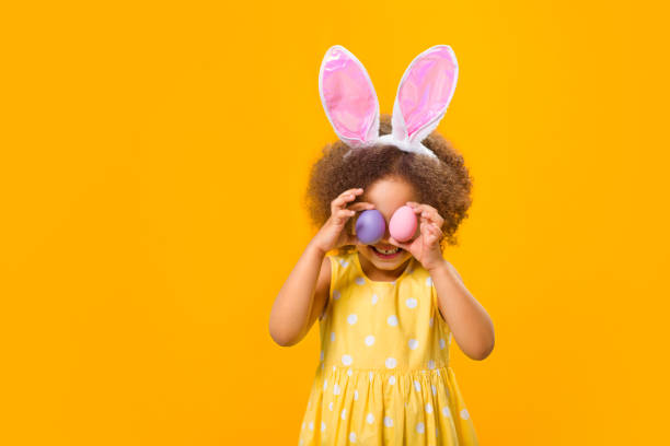 istock A a girl with rabbit ears on her head with painted eggs in her hands on a yellow background. 1369813041