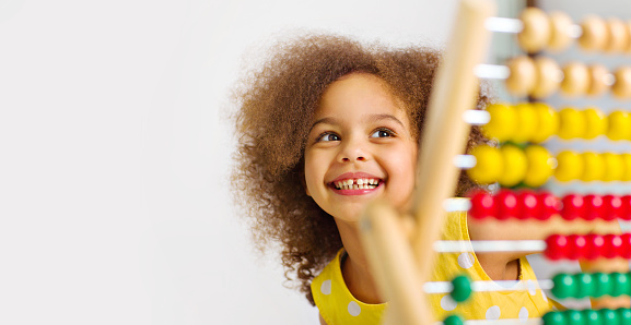 A Black girl is ready for a math and arithmetic lesson with an abacus. A a girl in a yellow dress counts an example in her mind. She holds a red pencil in her hand and smiles cheerfully