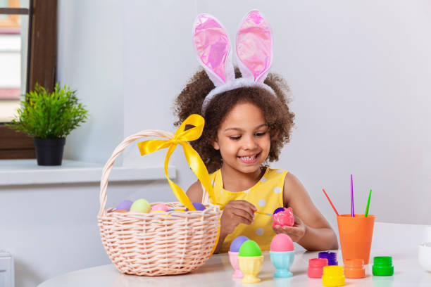 istock Little Black girl with bunny ears paint Easter eggs 1369813098