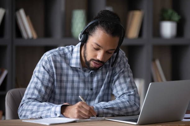 istock Focused student guy in headphones with mic writing notes 1369813848