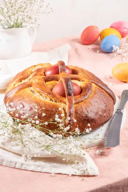 Photo of Portuguese traditional Easter cake. Folar with eggs on easter table. Blossom flowers and colorful painted eggs