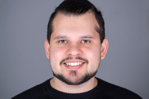 Young latin man studio frontal headshot smiling. He is in his 20s, has a small beard and short hair
