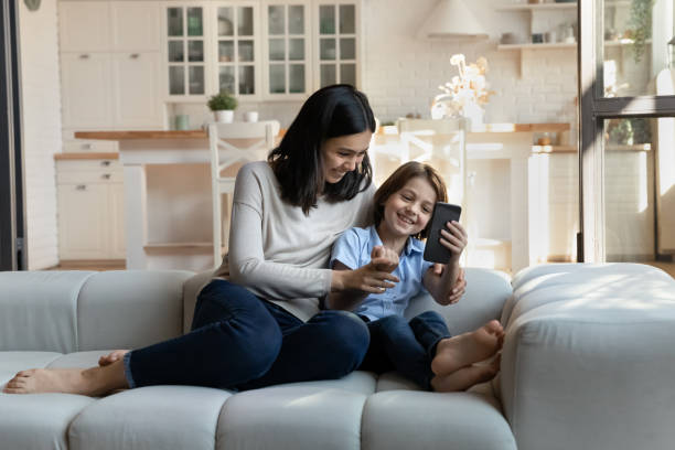 istock Cheerful mom and son sit on sofa with cellphone 1369822210