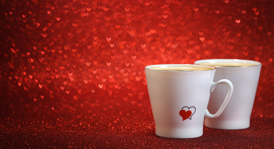 Two white coffee cups with red hearts filled in coffee.  Red glitter background with lots of hearts