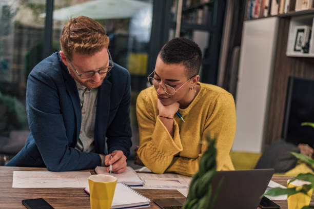 istock Two diverse natural colleagues in casual office or home office doing paperwork working together teaching, coaching or tutoring each other one another 1369825497