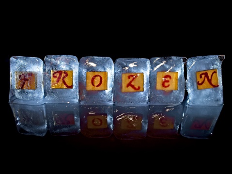 The word frozen spelled out in ice cubes illuminated using a light painting technique. A concept image on a black background with reflection useful for any idea on cold temperatures or frozen. Could be used for weather stories, relationship problems or even financial concepts such as frozen assets.