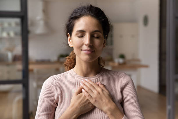 calm young woman hold hands on chest praying - mental health stockfoto's en -beelden