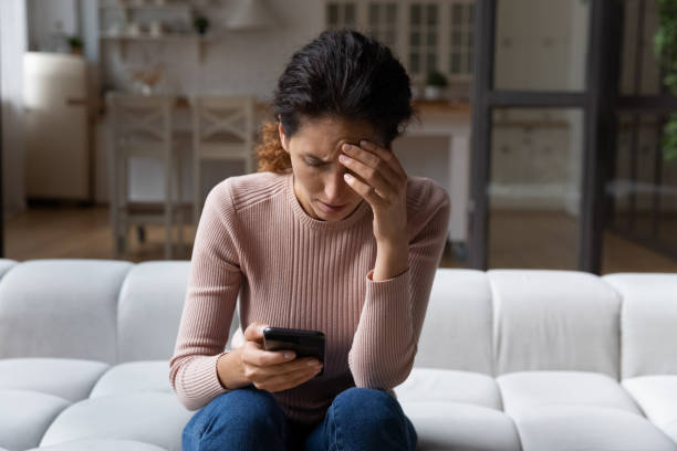 mujer infeliz usa teléfono inteligente angustiada con malas noticias - pessimist women one person caucasian fotografías e imágenes de stock