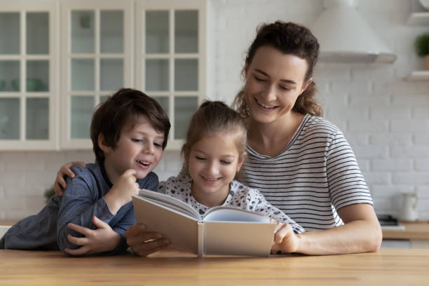istock Smiling little children reading book with caring mother. 1369841361