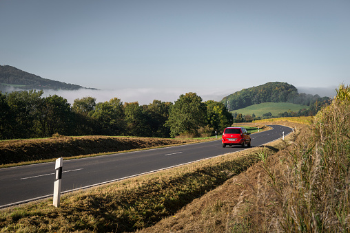 Poppenhausen, Germany - October 9, 2021: Red Ford Fusion driving into a fog wall on a road between agricultural fields under clear sky.