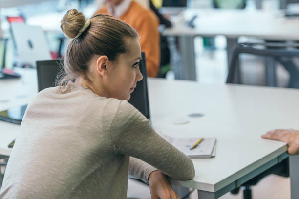 istock Blonde businesswoman working on her pc while sitting in a crowded modern office. 1369848487