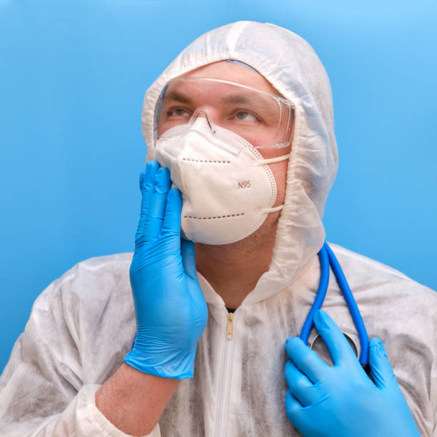 médico médico con un uniforme de traje protector con gafas y máscara facial sobre un fondo azul de estudio. paramédico con ropa protectora antiviral blanca con un respirador n95 y gafas de seguridad - doctor thinking asking pensive fotografías e imágenes de stock