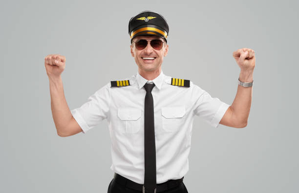 Happy male aviator in uniform and sunglasses smiling and keeping fists up while rejoicing over success against gray background