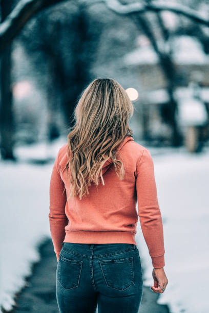 portrait de derrière une jeune femme caucasienne habillée de façon décontractée portant un sweat à capuche debout sur le trottoir par une froide journée enneigée - rear view women back back of head photos et images de collection