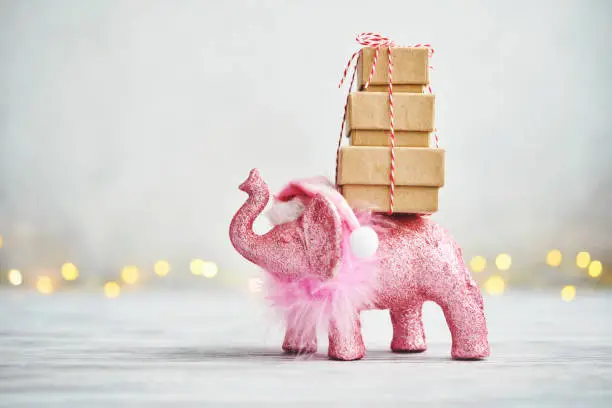 Photo of Holiday background with pink elephant wearing a Santa hat and carrying a stack of gifts for Christmas
