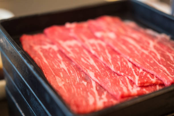 Fresh beef raw sliced with marbled texture served on black tray for Sukiyaki and Shabu