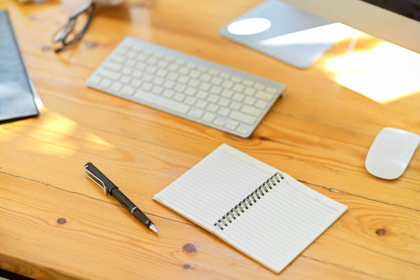 Modern office workspace with office supplies, stationery, wireless keyboard, pc desktop computer, an open empty spiral notepad on wooden table. close-up