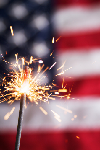 a firework sparkler close up with the American flag in the background. A Fourth of July concept. 