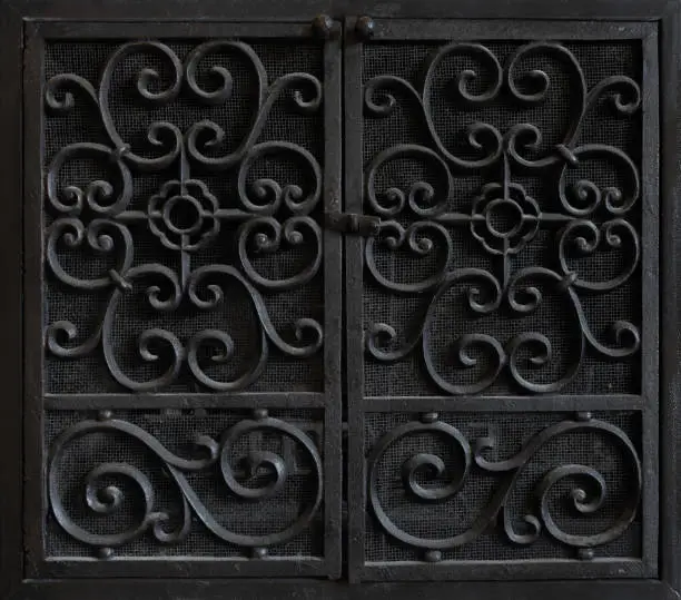 Black ornate door on hinges, opening in the middle.