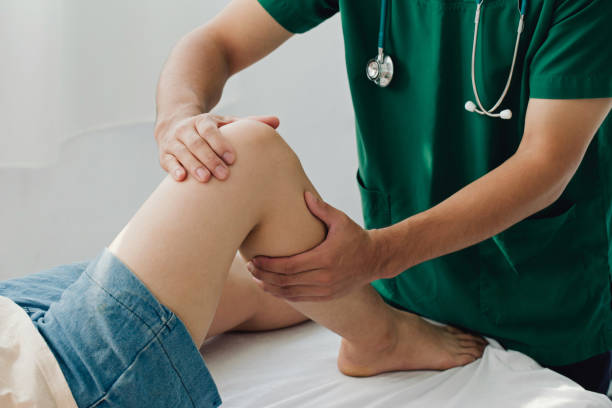 terapeuta de consulta com o tratamento do joelho lesionado do paciente com seu terapeuta em clínica, conceito de fisioterapia esportiva, - equipamento ortopédico - fotografias e filmes do acervo