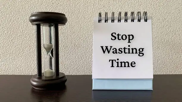 Photo of Stop wasting time text on notepad with minutes glass background. Conceptual.