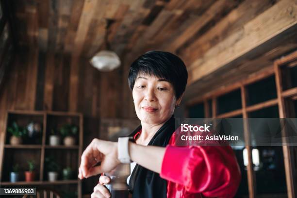 Active Senior Asian Woman Resting After Exercising At Home Looking At Her Smartwatch Using Fitness Tracker App And Measuring Pulse Maintaining Healthy Fitness Habits Elderly Wellbeing Health Wellness And Technology Concept Stock Photo - Download Image Now