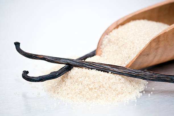 Cane sugar and Vanilla Beans Closeup of processed brown cane sugar in a wooden scoop and two vanilla beans or pods. VANILLA SUGAR stock pictures, royalty-free photos & images