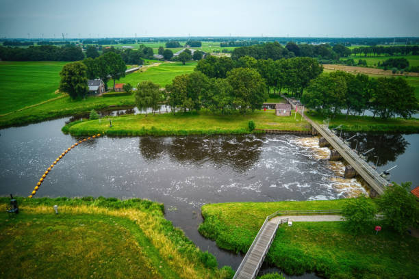 drone view of the river vecht, green grass, trees, beautiful blue sky and cycle path through the vecht valley. bridge and weir in the river. dalfsen netherlands - miniature weir imagens e fotografias de stock