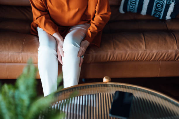 Cropped shot of a distraught senior Asian woman feeling unwell, suffering from pain in leg while sitting on sofa in the living room at home. Elderly and health issues concept Cropped shot of a distraught senior Asian woman feeling unwell, suffering from pain in leg while sitting on sofa in the living room at home. Elderly and health issues concept one senior woman only stock pictures, royalty-free photos & images