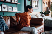 istock A distraught senior Asian woman feeling unwell, suffering from backache, massaging aching muscles while sitting on sofa in the living room at home. Elderly and health issues concept 1369889835