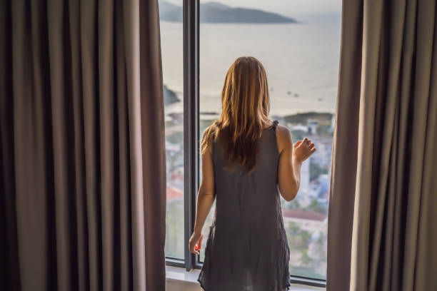 istock Young woman opens the curtains on a sea view window 1369889937
